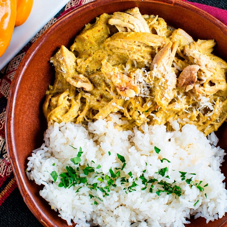 Bowl of white rice topped with chopped herbs and shredded chicken in a creamy green sauce, served beside orange peppers.